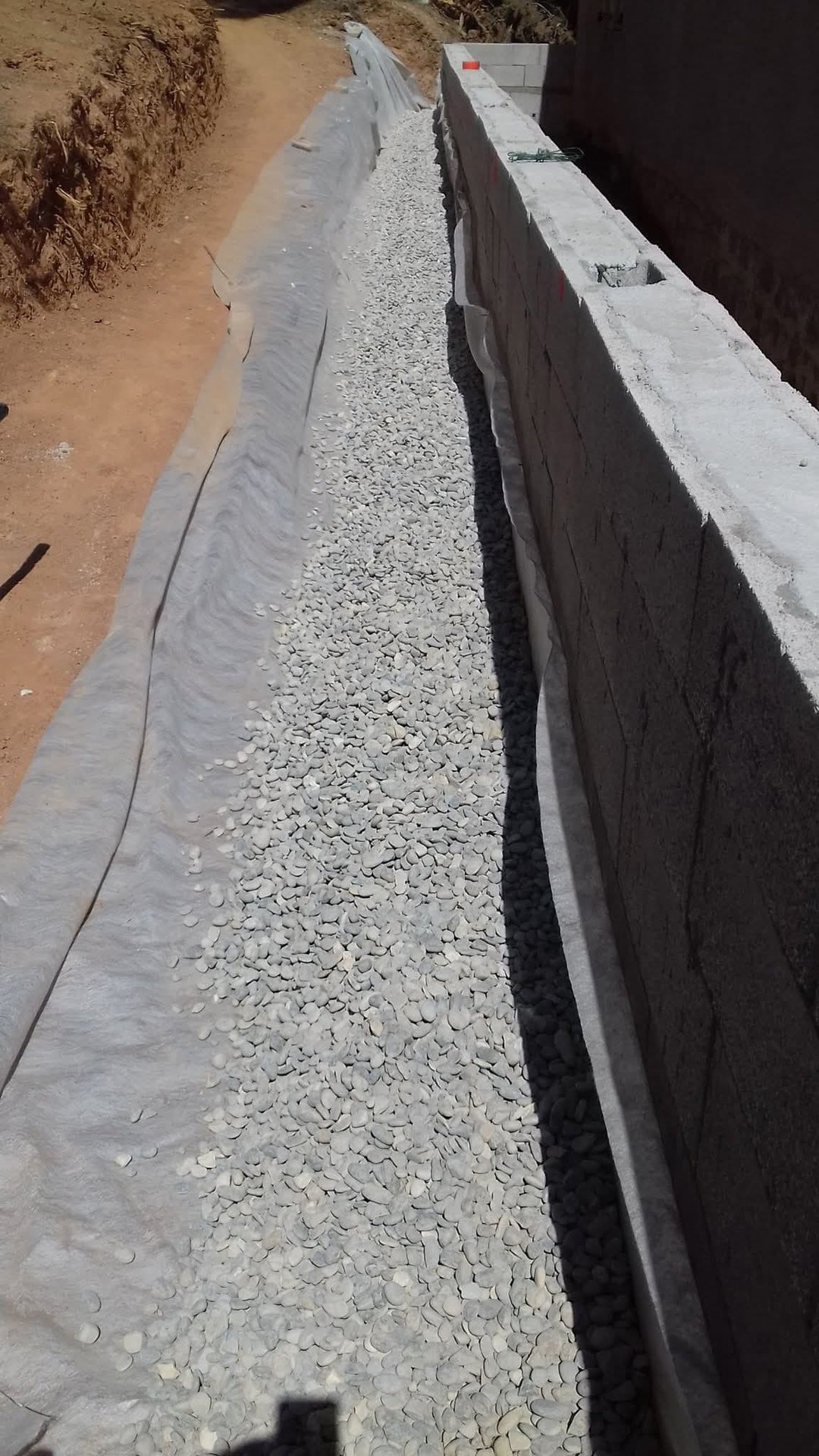 Pose d'un drain agricole en tranchée avec géotextile et lit de gravier le long d'un mur de fondation